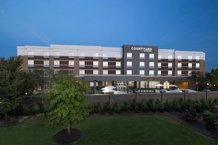Hotel exterior at dusk with a four-story building labeled "Courtyard." Warm lighting highlights outdoor seating and lush greenery enhances the serene ambiance.