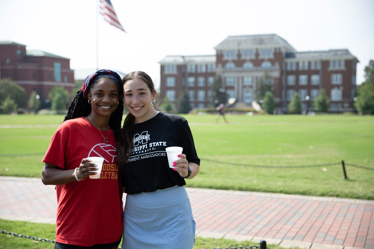 Two MSU students standing on the Drill Field on a sunny day smiling at the camera