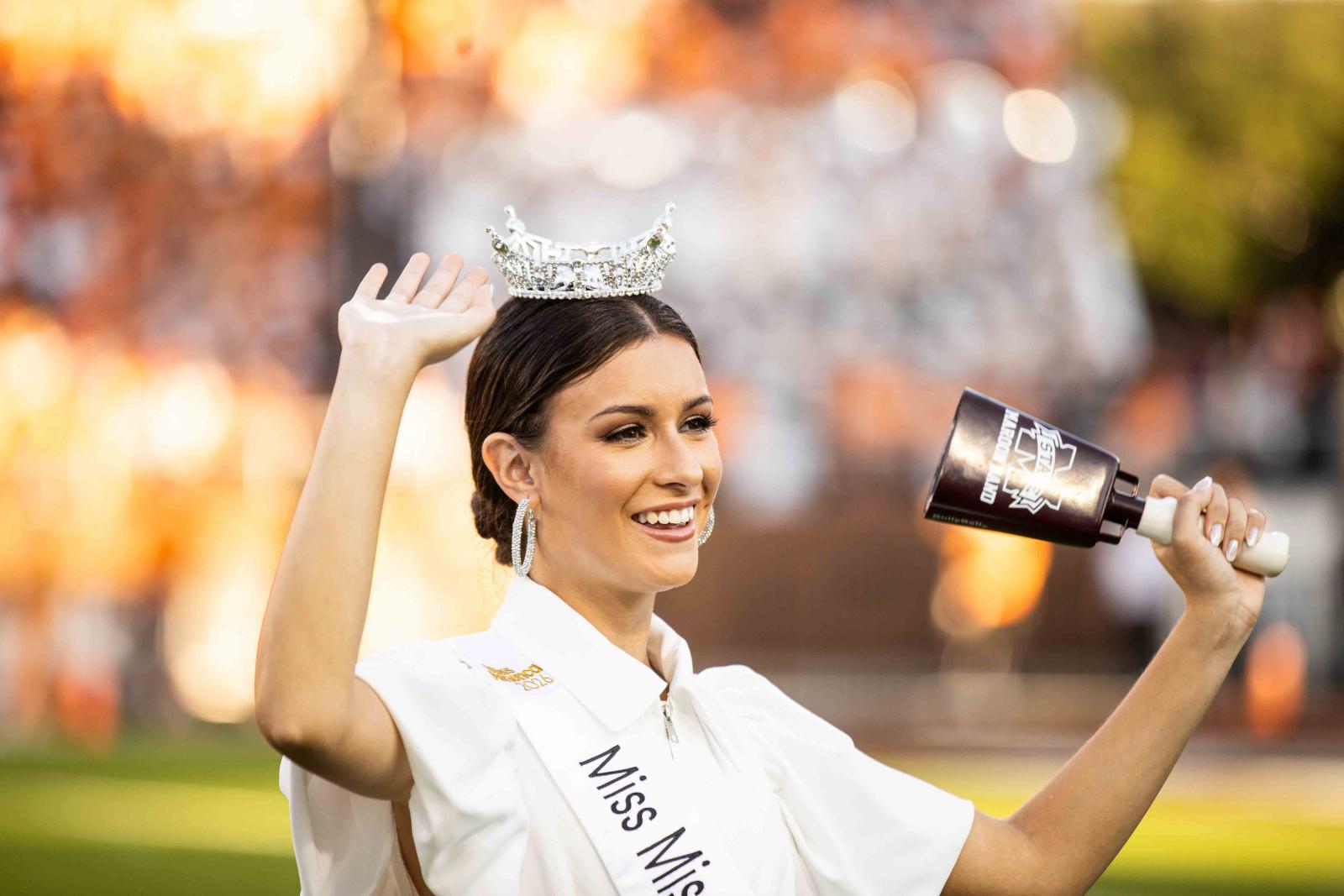 Young woman wearing a crown and white sash is smiling