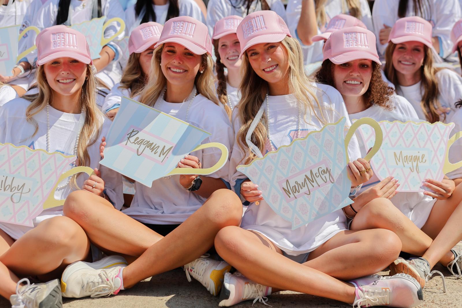 A group of young women in matching pink hats and white shirts sit on the ground