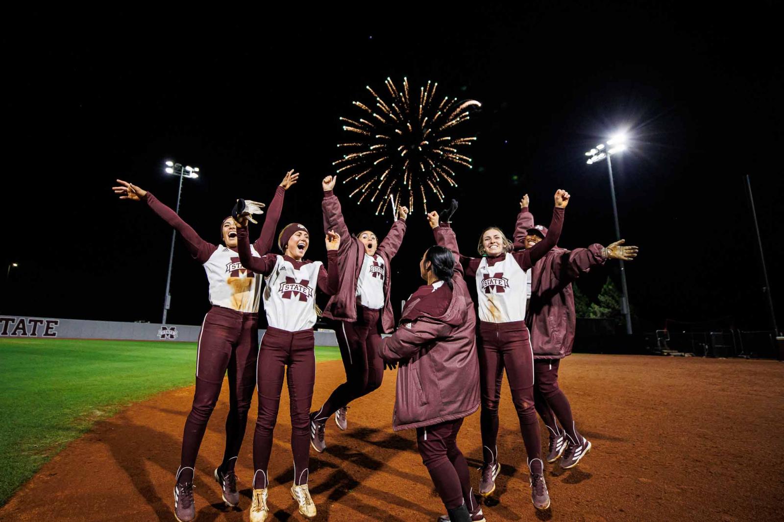 Mississippi State womens softball team jumping on the field in front of fireworks.