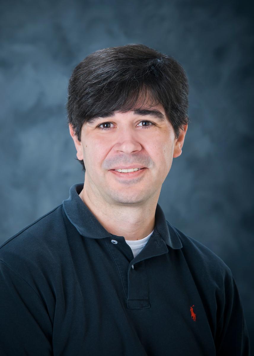 Portrait of Shannon Newell with short dark hair wearing a black polo. 