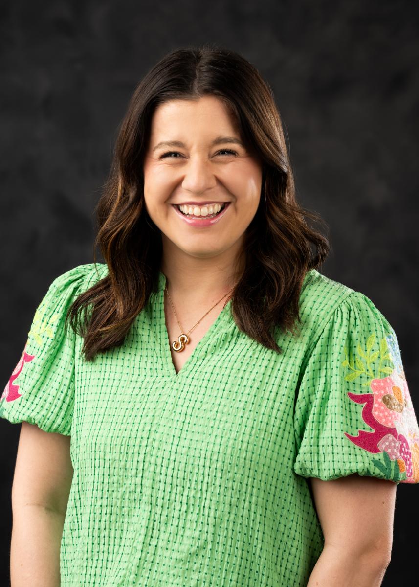 women with brown hair smiling at the camera in a green top 