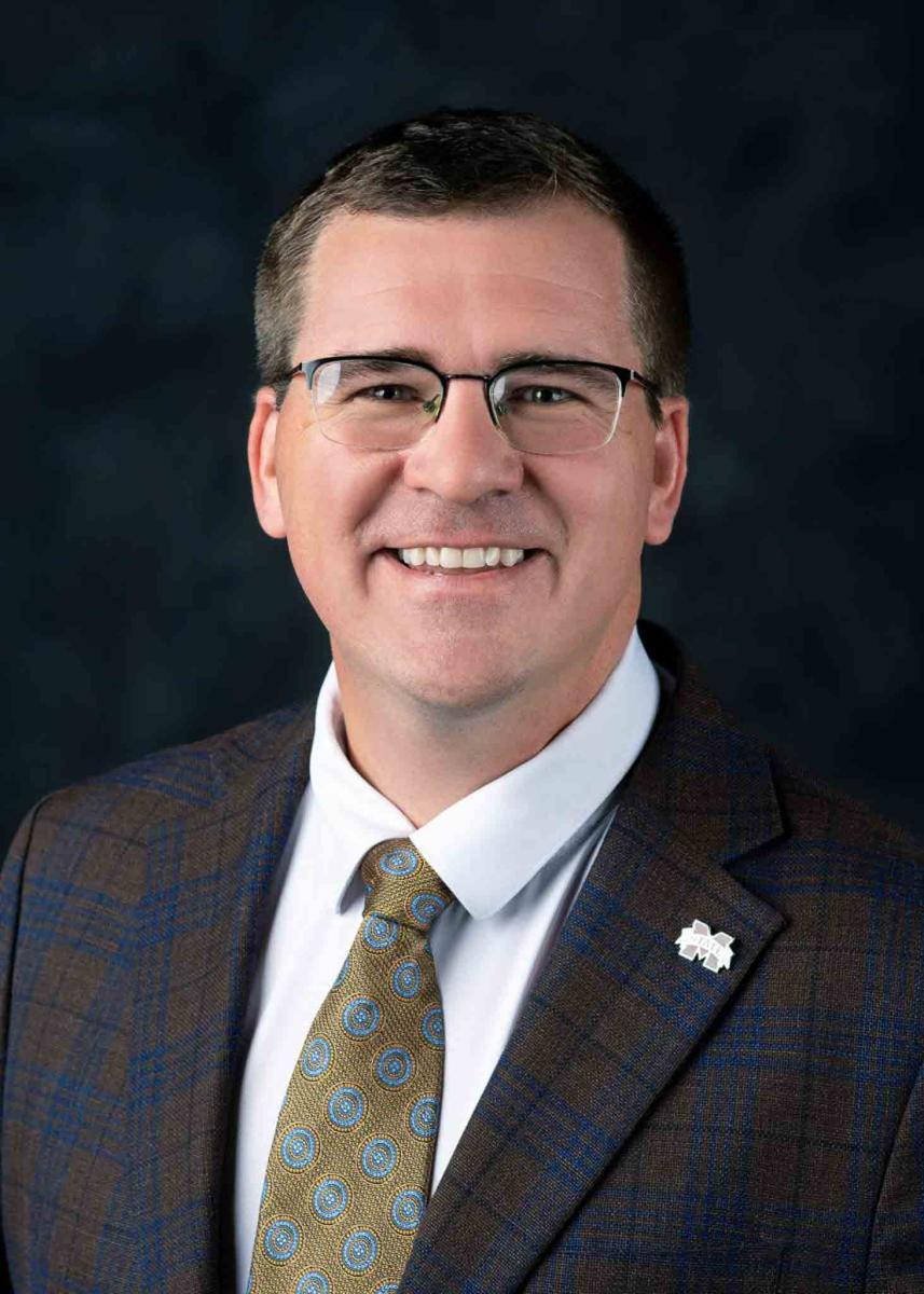 Mississippi State University professional headshot of a man with dark hair and glasses wearing a tie and a suit jacket. 